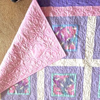 Quilt with purple and pink geometric design.